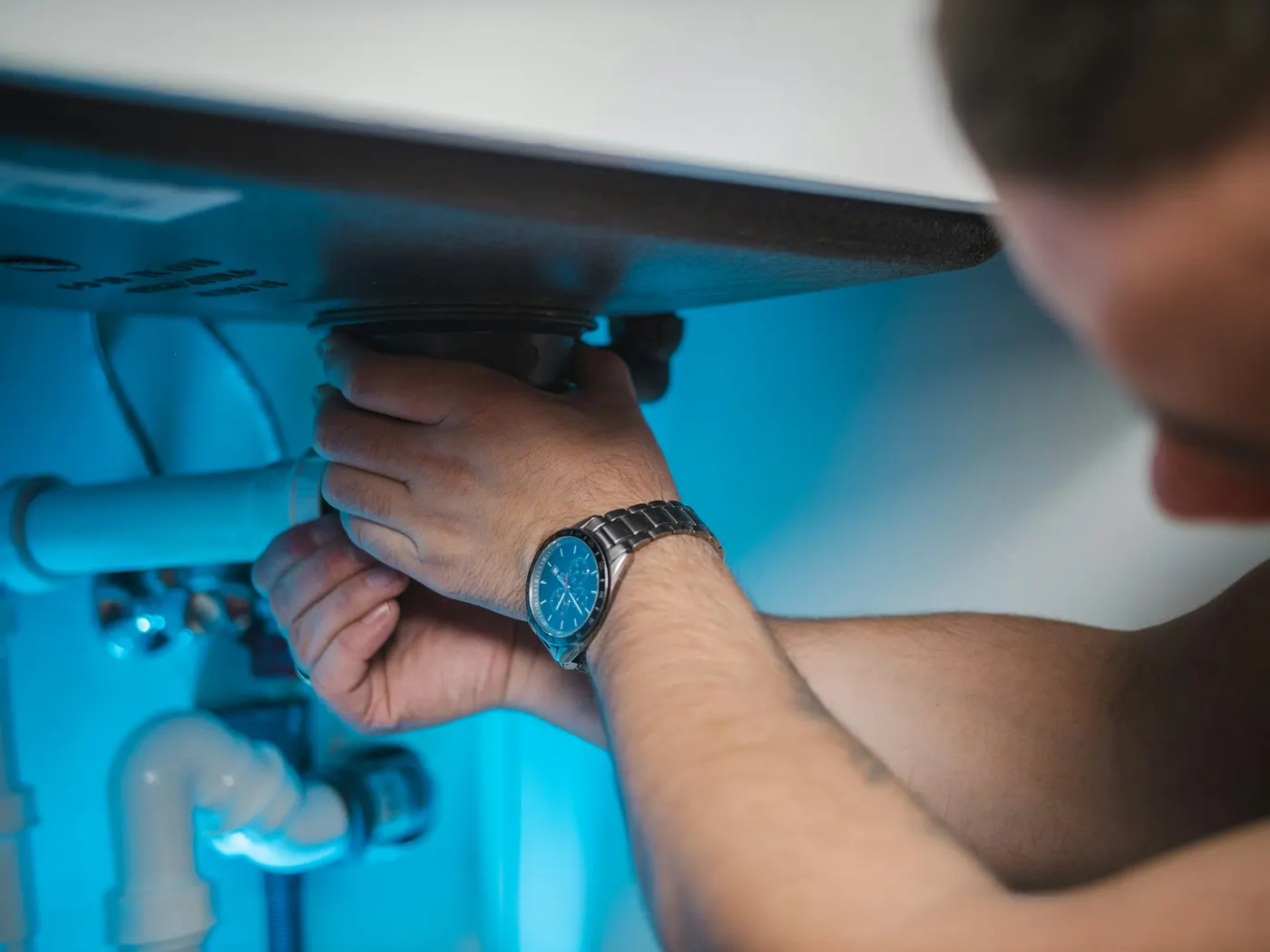 A plumber working on the plumbing under a sink